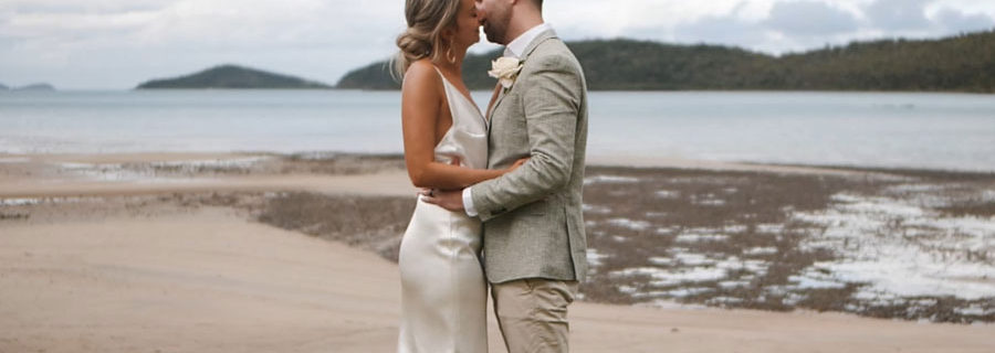 bride and groom kissing on lawn next to beach