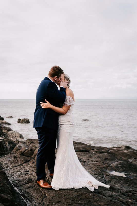 bride and groom next to the ocean kissing