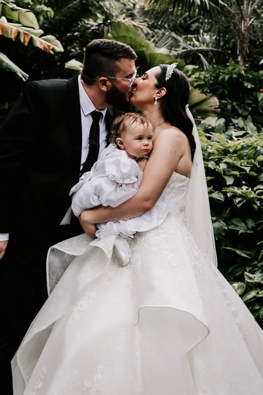 bride and groom kiss with daugher
