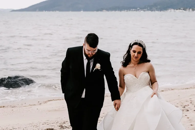 bride and groom hold hands and walk on beach