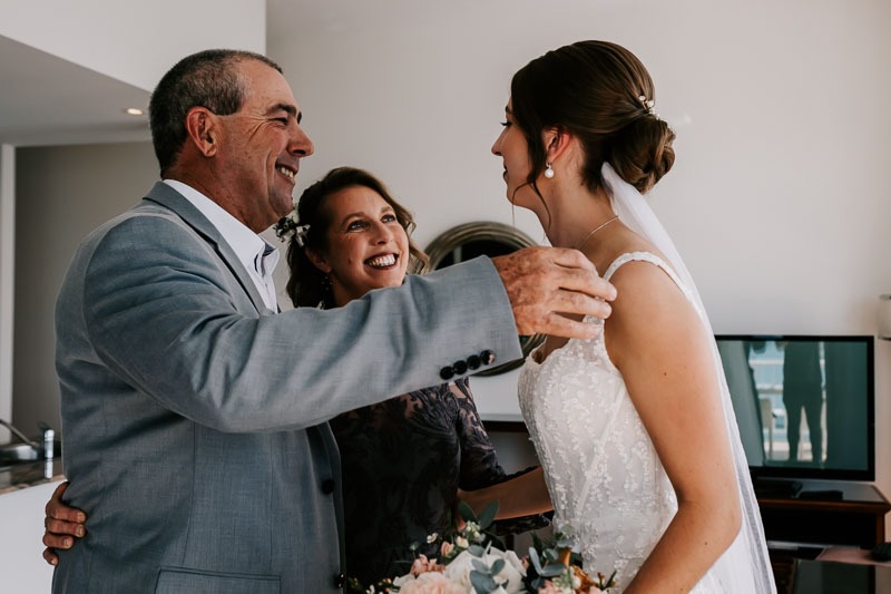 father and mother leaning in to hug bride