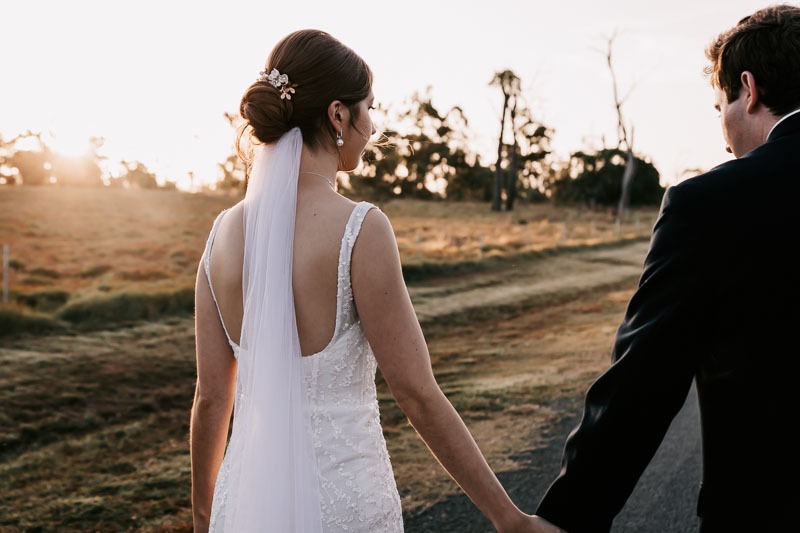 bride holding hands with groom in feild with sunset