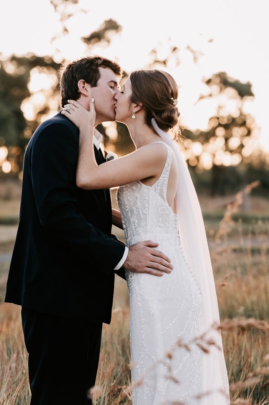 bride and groom kiss in field