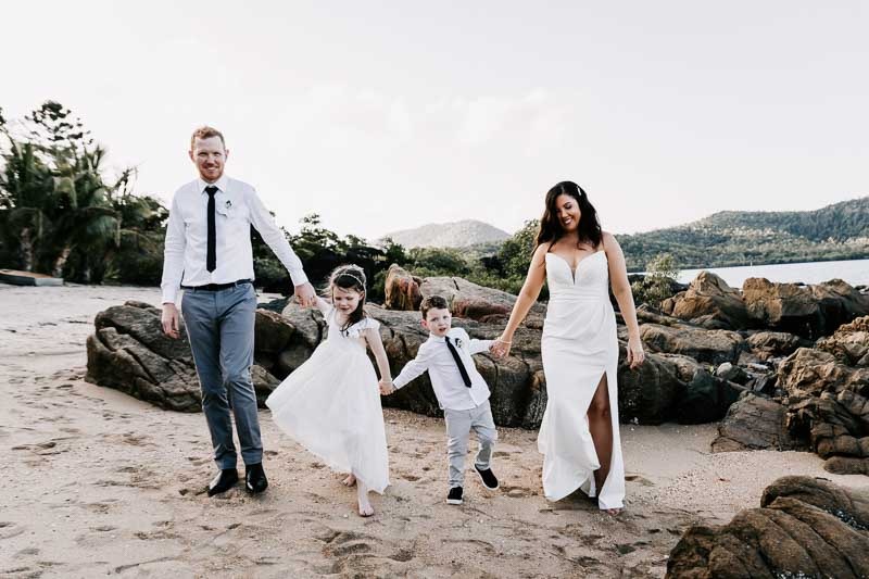 Bride & Groom holding hands with children on beach
