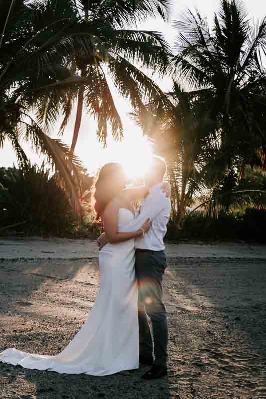 Bride & Groom embrace on the sand with sun behind them