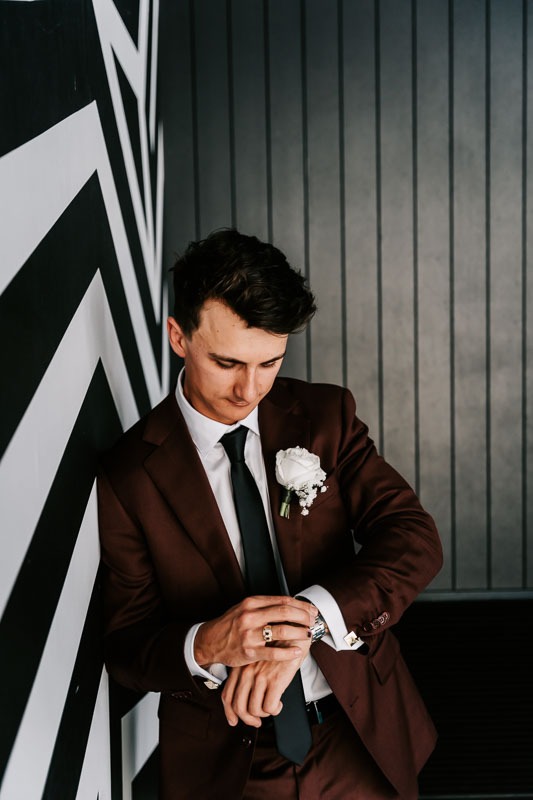 Groom checking watch leaning against wall