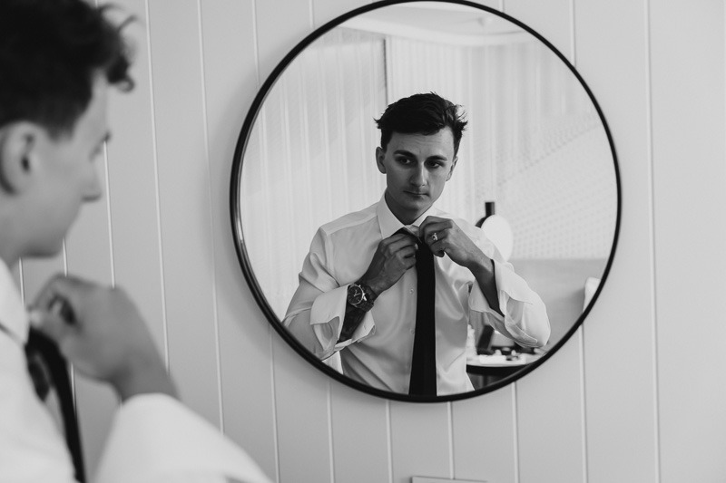 Groom in mirror putting on tie