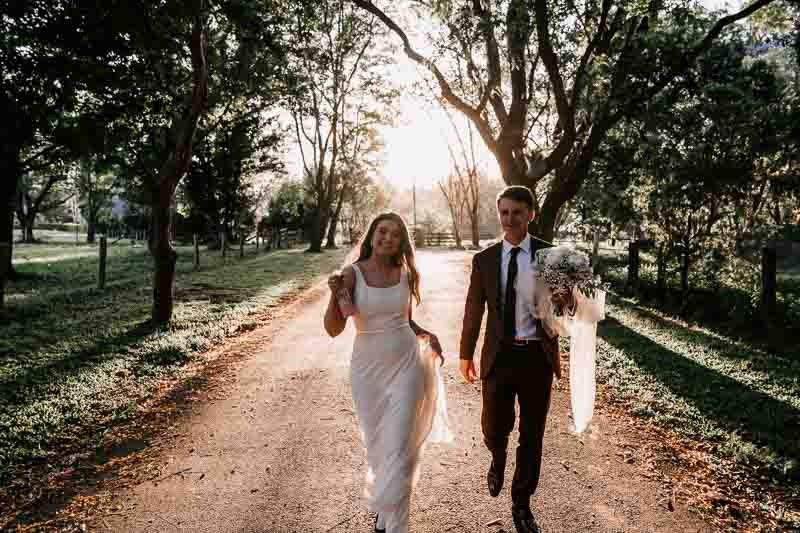 Bride & Groom dance down road with sunset behind them