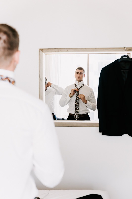 Groom putting on tie in mirror reflection