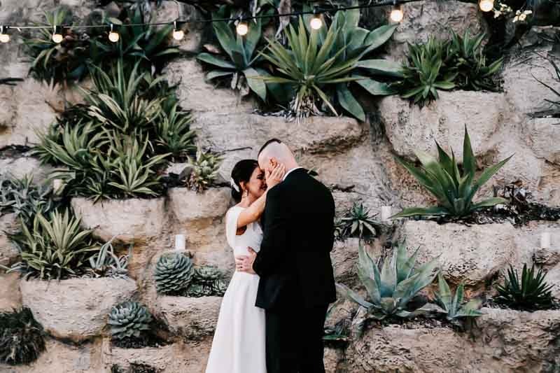 Bride & Groom dance with succulent wall behind them