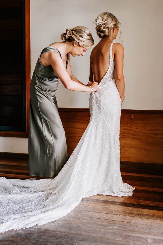 Bridesmaid helps Bride into dress