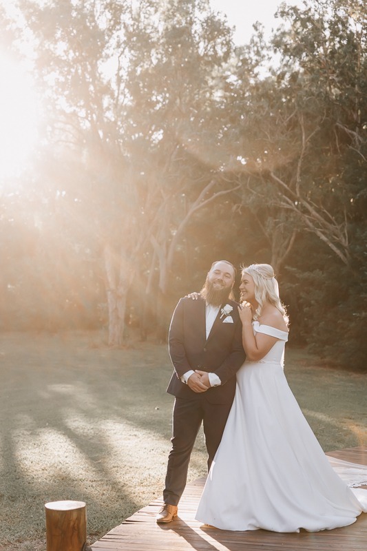Bride & Groom embrace with sunlight leaking through trees