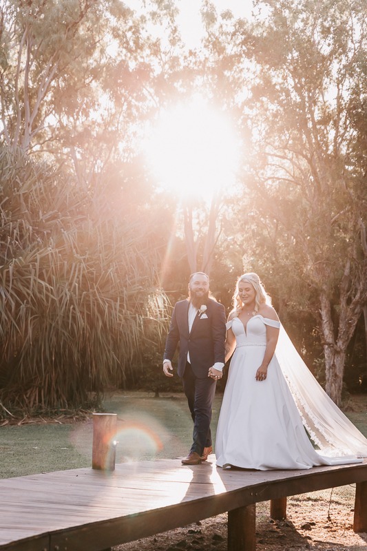 Bride & Groom embrace with sunlight leaking through trees