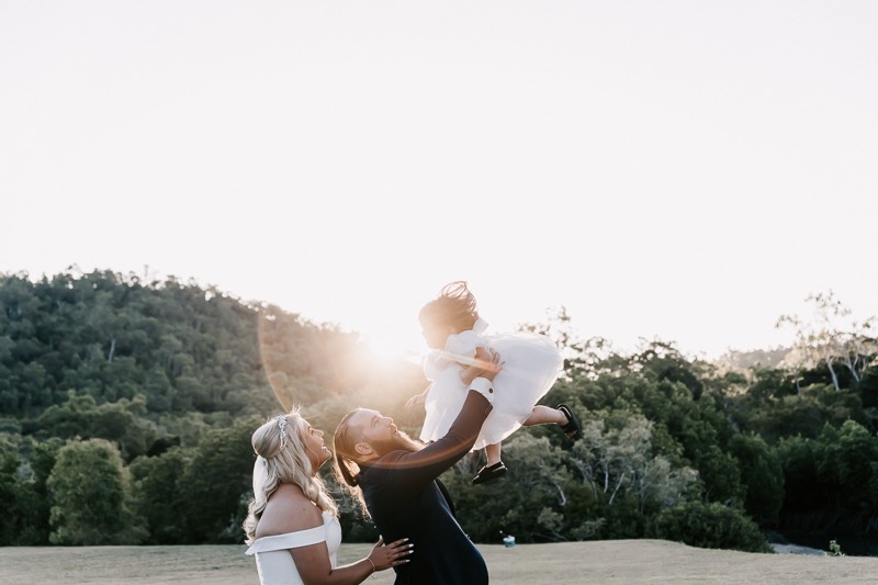 Groom lifts daughter over head in sunset