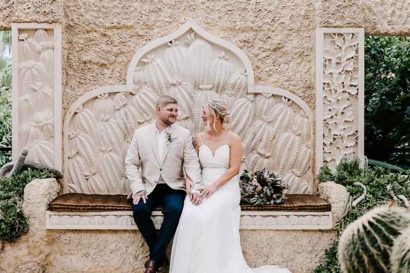 Bride & Groom sit on bench and smile at eachother