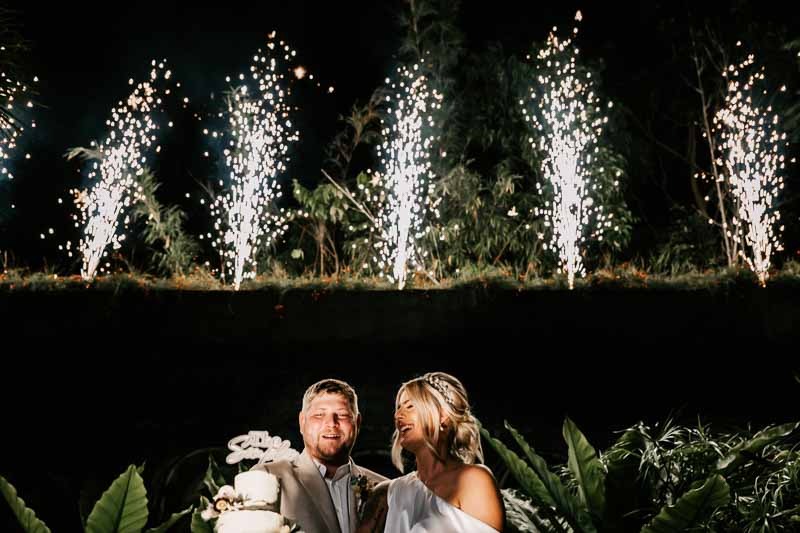 Bride & Groom cut cake with fireworks behind