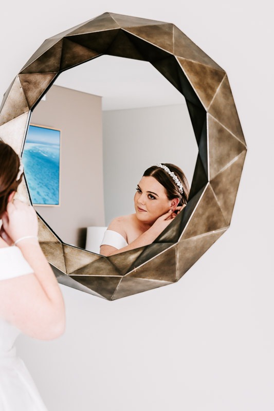 Bride putting on earrings in mirror