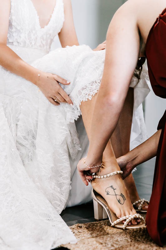 Bridesmaid helping Bride put on shoes
