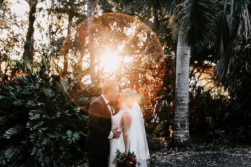 Bride & Groom embrace and kiss with sun flare