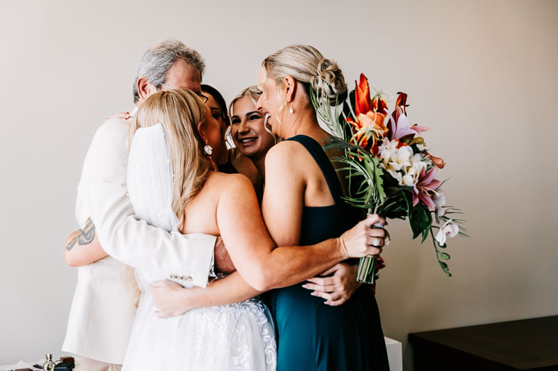 Bride embracing bridesmaids and father