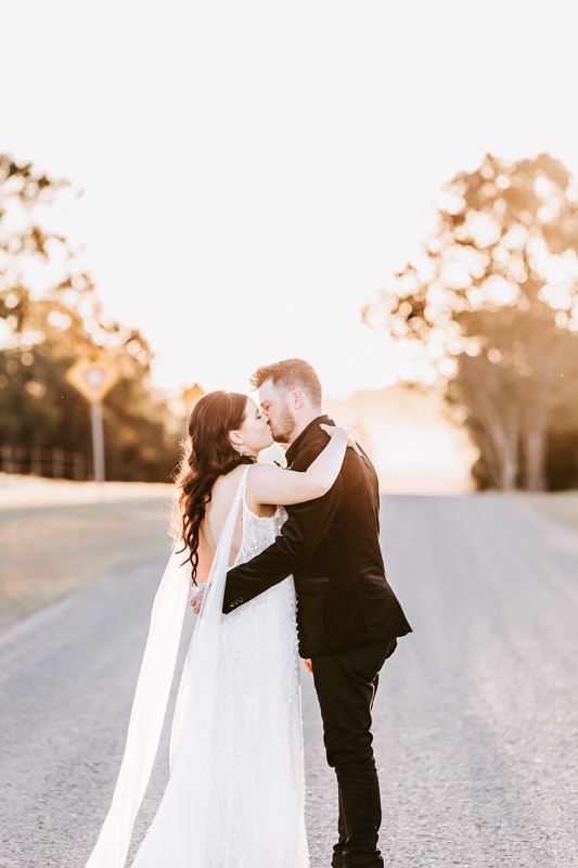 Bride & Groom kiss on dirt road at sunset