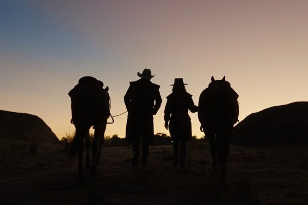 two peopleand their horses as silhouette wearing drizabone