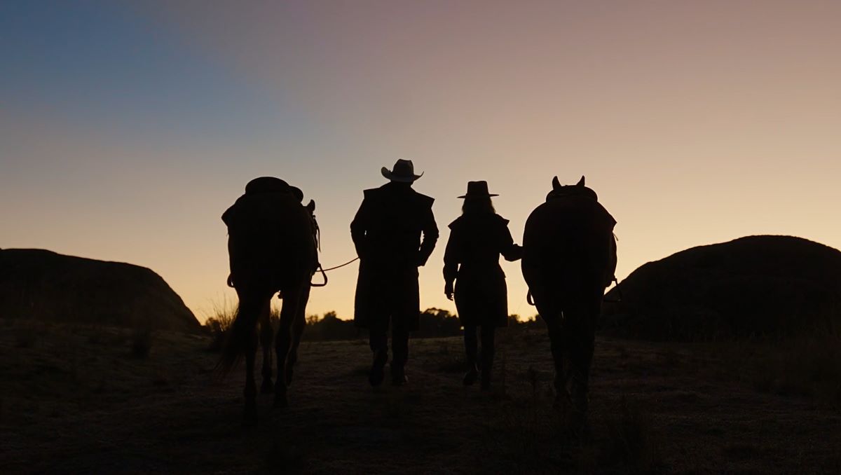 two peopleand their horses as silhouette wearing drizabone