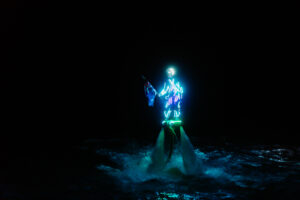 Professional videography, photography, and drone footage of lit performer over water.