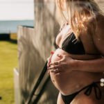 Maternity photography – close-up of pregnant woman holding belly outdoors