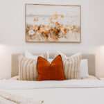 Bedroom with rust-coloured cushions and floral artwork