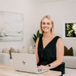 The Stylist seated at a kitchen bench with a laptop