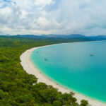 Professional videography, photography, and drone footage of a scenic coastline with lush greenery and turquoise waters.