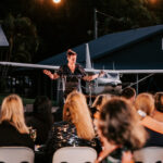 Professional videography at outdoor event with small airplane backdrop