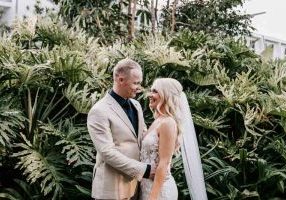 Bride and Groom embrace with green bush behind